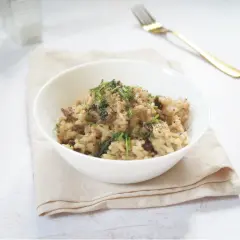 Miseczka kremowego risotto z grzybami, posypana ziołami, na jasnym obrusie.