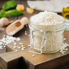 Słoik z ryżem do risotto, obok czosnek, bazylia i oliwa.