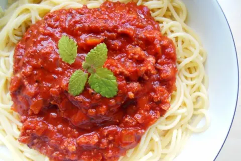 Spaghetti z bogatym sosem pomidorowym i mięsem mielonym, udekorowane listkami mięty.