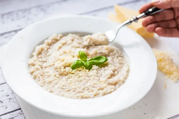 Kremowe risotto z parmezanem i bazylią na białym talerzu, widok z góry.