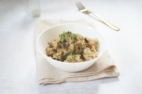 Miseczka kremowego risotto z grzybami, posypana ziołami, na jasnym obrusie.