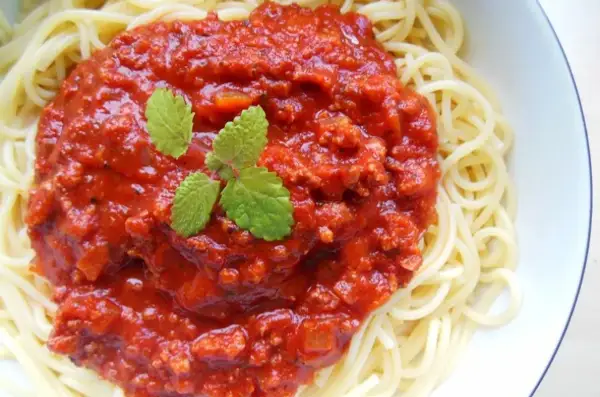 Spaghetti z bogatym sosem pomidorowym i mięsem mielonym, udekorowane listkami mięty.