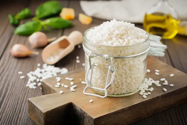 Słoik z ryżem do risotto, obok czosnek, bazylia i oliwa.